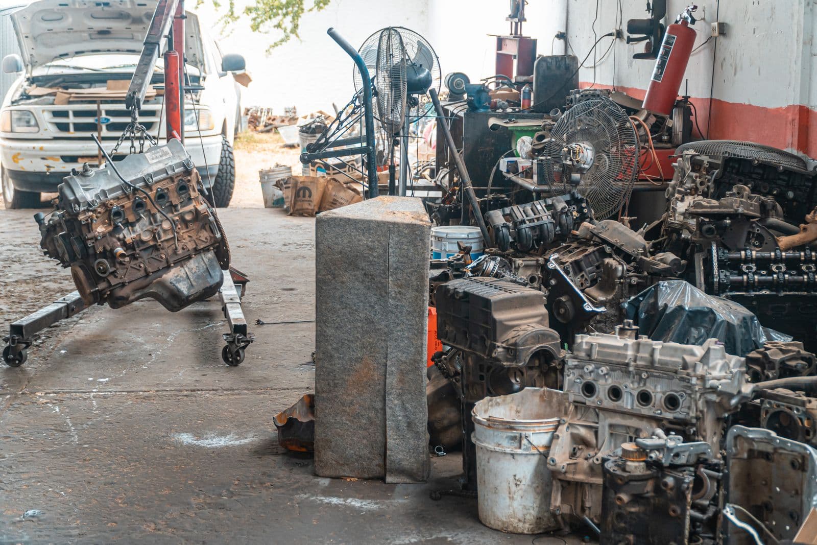Stripped engines on stands in a workshop, one lifted on an engine crane
